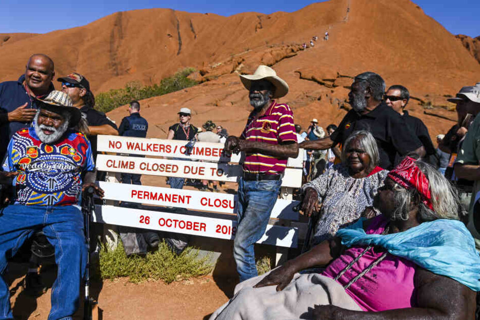 Aborigines stehen für ein Foto neben einem neu installierten Schild mit dem auf die Schließung eines Kletterwegs am Uluru, auch bekannt als Ayers Rock, im Uluru-Kata Tjuta Nationalpark hingewiesen wird.