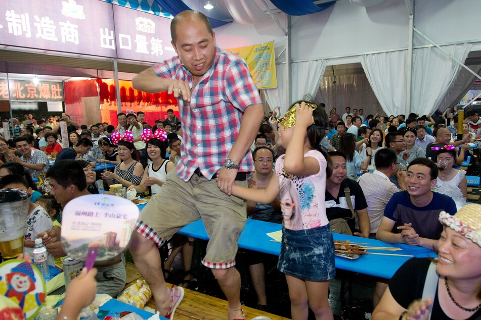 Ein Besucher tanzt beim Oktoberfest im chinesischen Qingdao in einem Festzelt auf einer Biertischgarnitur. (Archivbild)