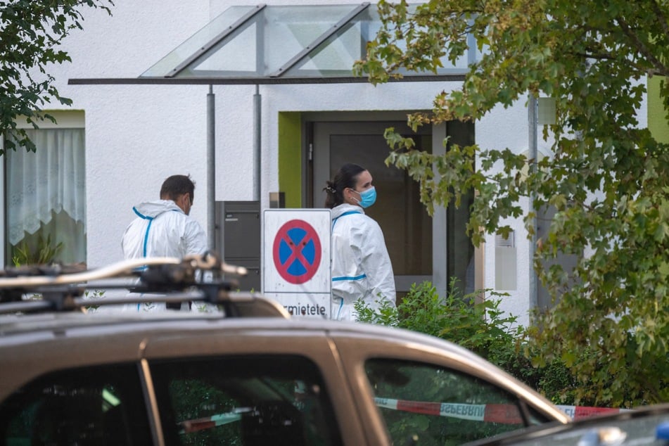 Polizisten stehen vor einem Mehrfamilienhaus, in dem zwei Tote in einer Wohnung gefunden wurden.