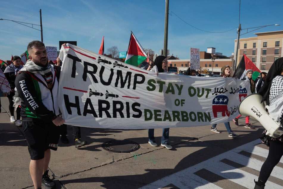 Pro-Palestine and Lebanon demonstrators march with a banner against Republican presidential nominee Donald Trump and Democratic nominee Kamala Harris during a "No Vote for Genocide" protest in Dearborn, Michigan.