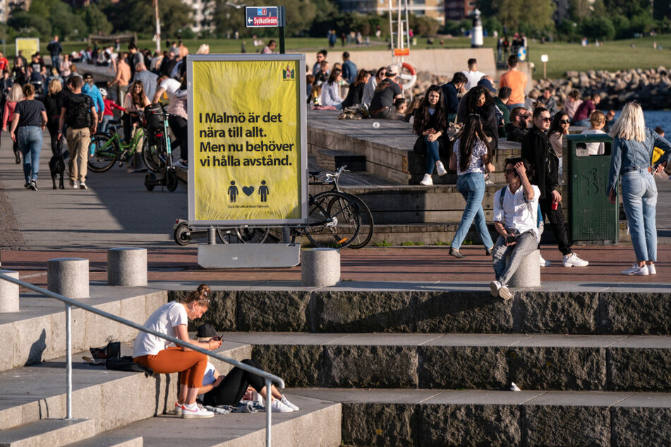 26. Mai 2020, Malmö: Menschen genießen das warme Abendwetter hinter einem Schild, das sie darauf hinweist, Abstand zu halten.