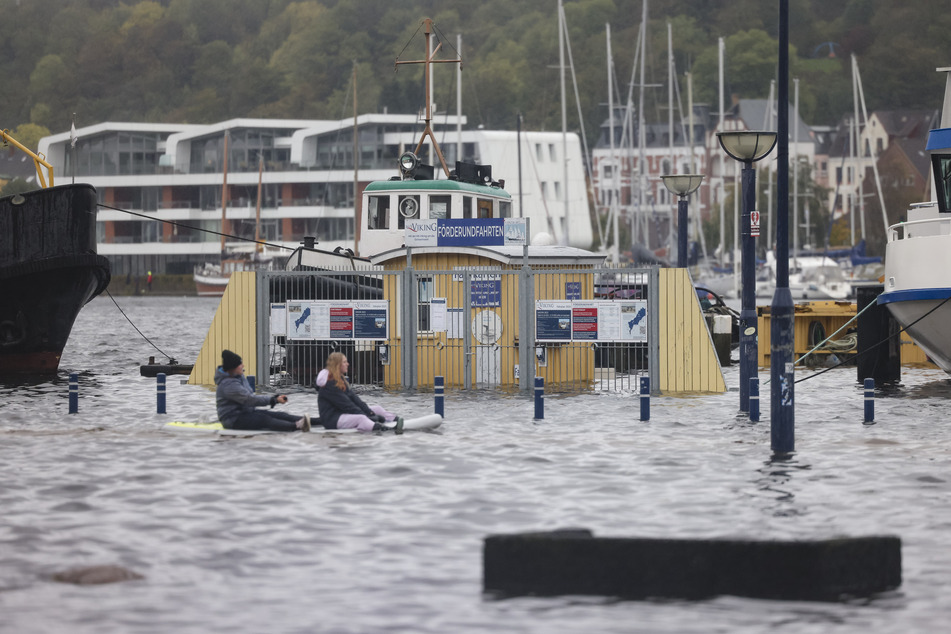Zwei Personen bewegen sich auf einem Stand-Up-Paddle Board fort. Das Hochwasser überschwemmte Teile von Flensburg.