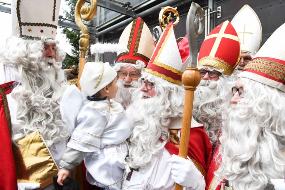 Sechs Mitglieder der Nikolausgilde stehen als Nikoläuse verkleidet nach einem Gottesdienst vor der katholischen Kirche zusammen. (Archivbild)