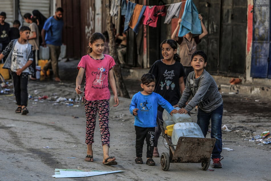 Palästinensische Kinder tragen gefüllte Wasserbehälter, nachdem sie Schlange gestanden haben, um sie mit Trinkwasser zu füllen.