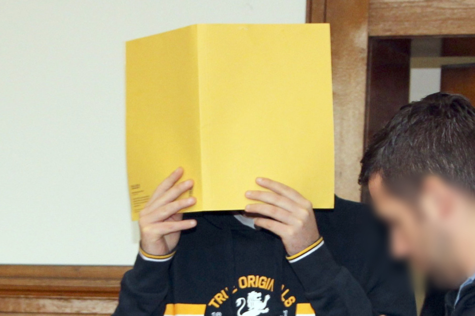 Der 40-Jährige versteckt sein Gesicht hinter einer Mappe.