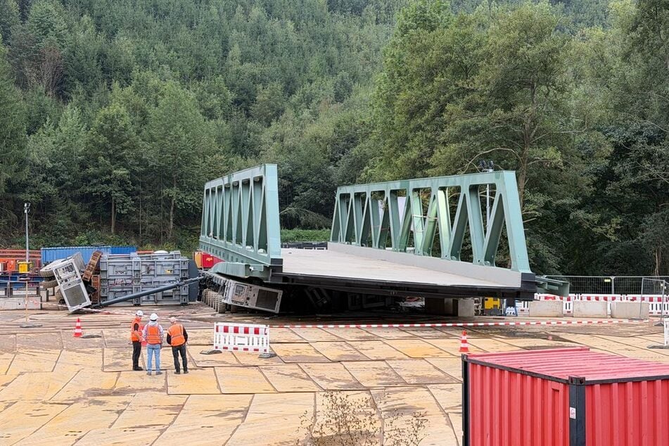Arbeiter stehen vor der abgesackten Stahlbrücke in Kirchhundem (NRW).