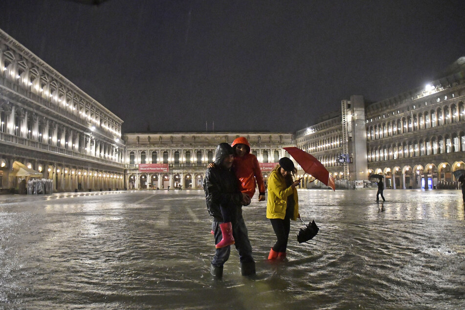 Drei Menschen laufen über dem komplett überfluteten Markusplatz in Venedig.