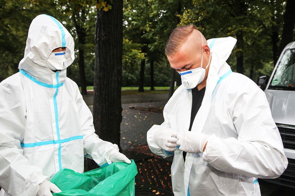Zwei Soldaten ziehen ihre Schutzkleidung aus, nachdem sie einen Abstrich bei einer Corona-Verdachtsperson genommen haben.
