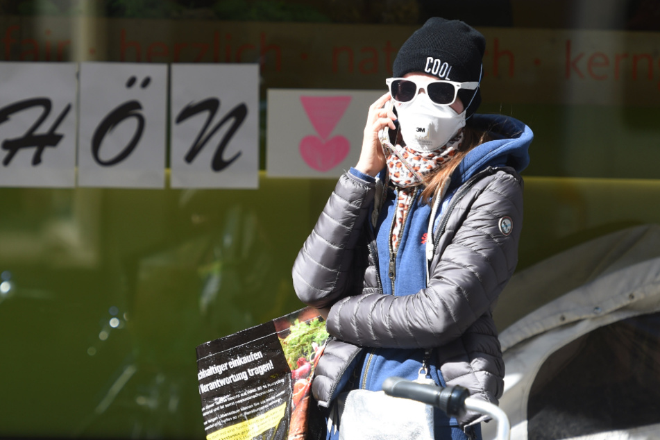 Eine Passantin steht in München mit Mundschutz und Sonnenbrille vor einem Laden und telefoniert.
