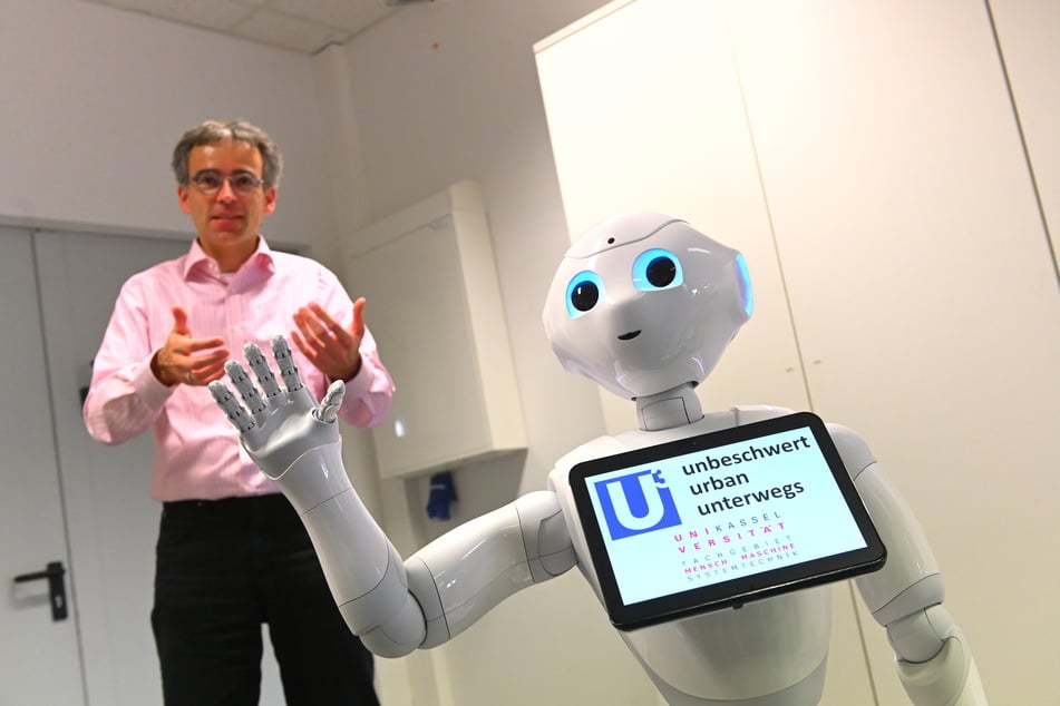 Professor Ludger Schmidt steht hinter Roboter Pepper. Der Roboter ist Teil des millionenschweren Forschungsprojekts "Unbeschwert urban unterwegs" (U-hoch-3).
