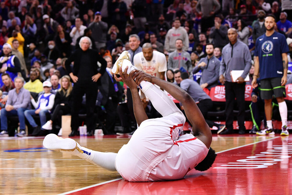The Sixers' Joel Embiid writhes in agony after rolling his ankle against the Timberwolves.