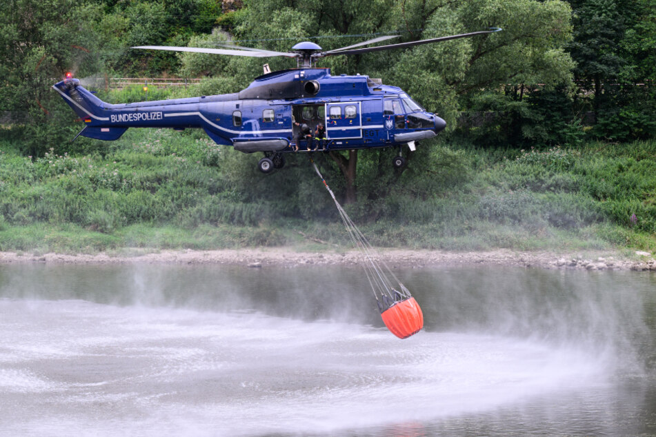 Ein Hubschrauber der Bundespolizei nimmt mit einem Löschwasser-Außenlastbehälter aus der Elbe Wasser auf.