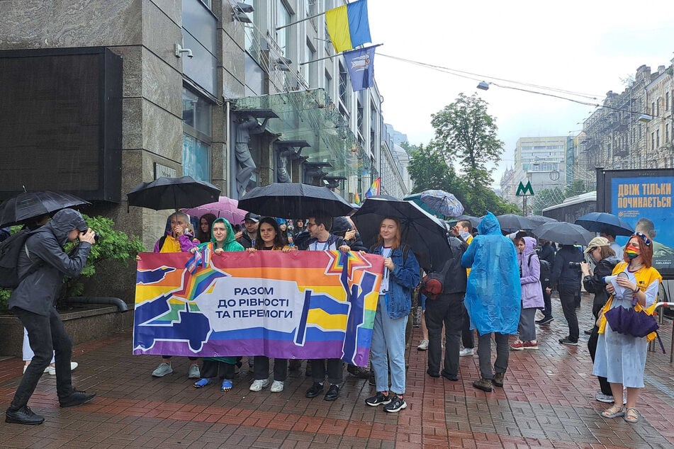 Menschen versammeln sich zu einer Pride-Kundgebung, sie halten ein Plakat mit der Aufschrift "Gemeinsam zur Gleichheit und zum Sieg".