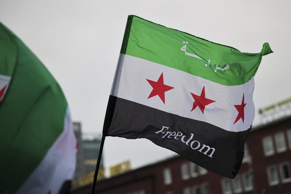 Feiernde schwenken die Flagge der syrischen Revolution vor einem Hauptbahnhof in Deutschland. (Archivbild)