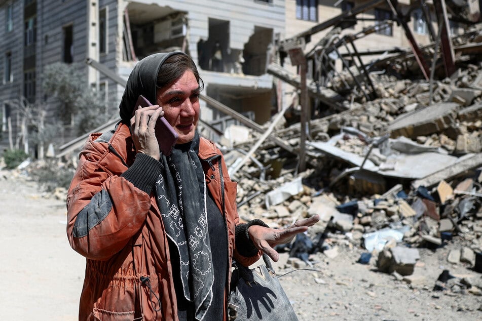 A woman talks on the phone while standing amid a damaged residential neighborhood in Tehran hit by a strike amid the US-Israeli war on Iran on March 30, 2026.