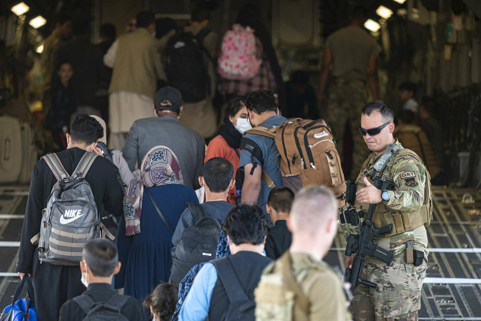 An Air Force airman assists Afghan refugees board an Air Force C-17 Globemaster III aircraft.