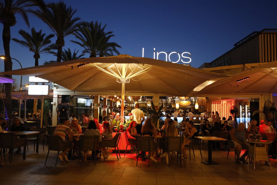 Menschen sitzen in einer Bar an der Strandpromenade von Palma. auf Mallorca sind die Corona-Zahlen wieder in die Höhe geschossen.