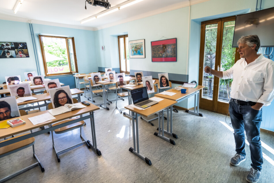 Schweiz, Sion Sitten: Der Lehrer Christophe Blanc gibt per Videokamera in einem Klassenzimmer mit Bildern seiner Schüler in der Privatschule "Ecole Ardevaz" Wirtschaftsunterricht. Die Schweiz beginnt rund sechs Wochen nach dem Schließen der meisten Geschäfte mit einer Lockerung der Corona-Schutzmaßnahmen.