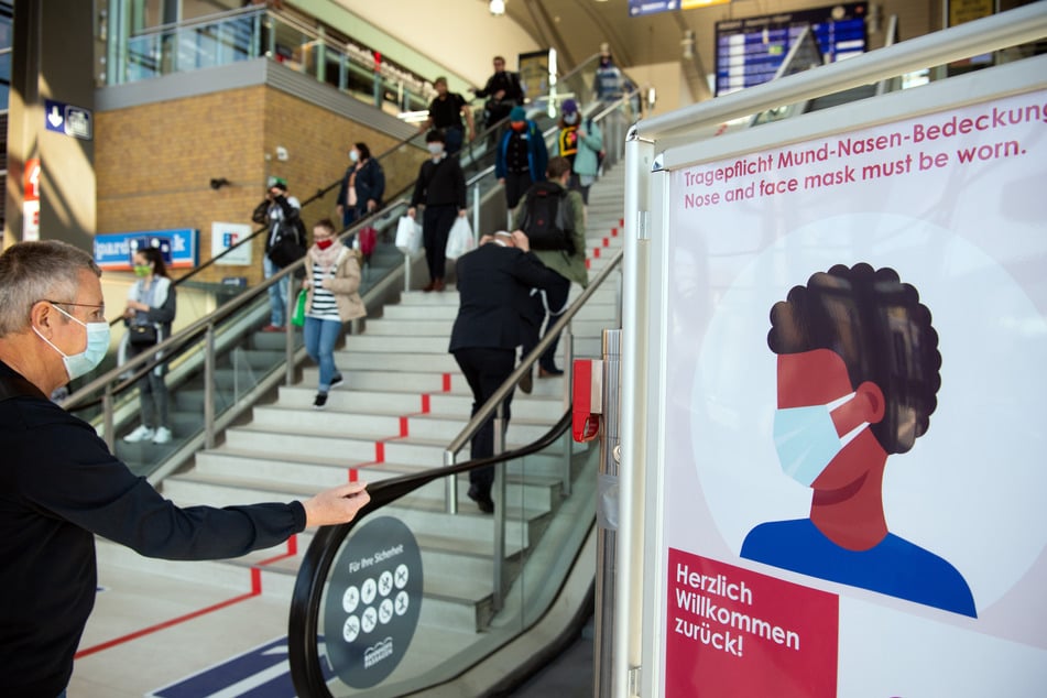 Passanten mit Mundschutz gehen im Hauptbahnhof an einem Schild der Bahnhofs-Passagen mit der Aufschrift "Herzlich willkommen zurück! Tragepflicht Mund-Nasen-Bedeckung." vorbei.
