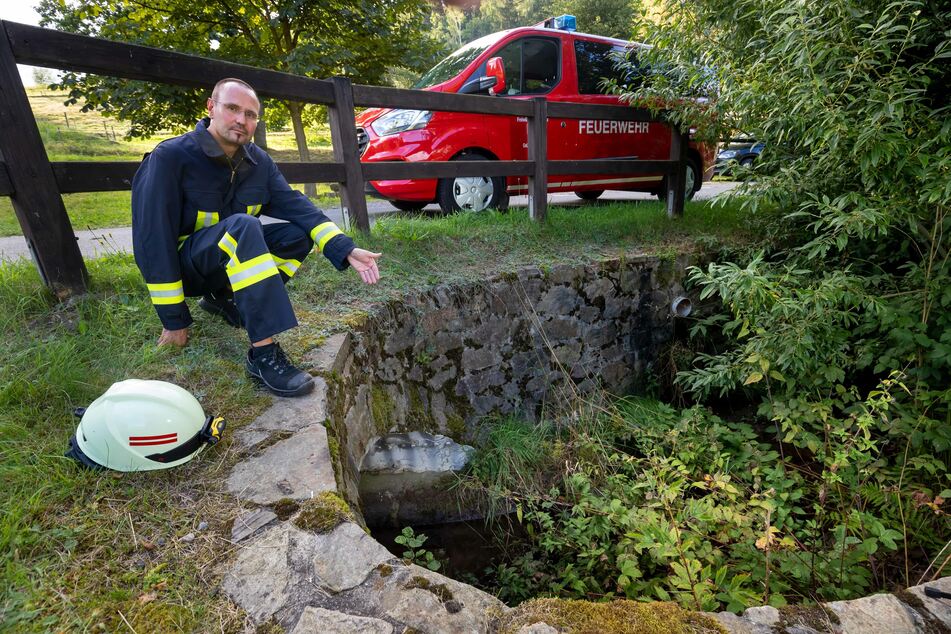 Gunnar Ullmann (44) vom Kreisfeuerwehrverband Erzgebirge zeigt auf den leeren Trübebach in Grünhainichen.