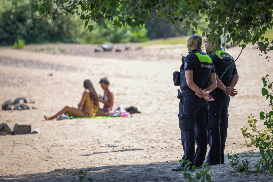 Mitarbeiter vom Ordnungsamt der Stadt Düsseldorf stehen an einem Strandabschnitt des Rheins und überwachen das Badeverbot.