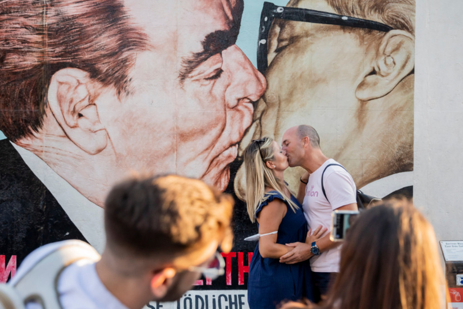 Berlin: Ein Paar lässt sich an der East Side Gallery vor dem Gemälde "Bruderkuss zwischen Leonid Breschnew und Erich Honecker" beim Küssen fotografieren.