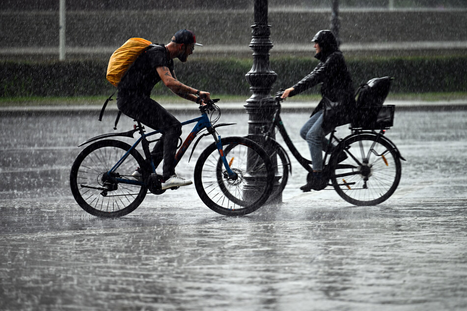 Ein Bild, wie man es dieser Tage häufig sieht: Zwei Fahrradfahrer begegnen sich bei starkem Regen an der Siegessäule auf der Straße des 17. Juni in Berlin.