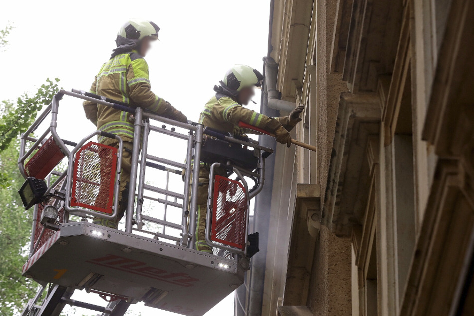 Zwei Feuerwehrmänner vor einem Fenster im zweiten Stock.