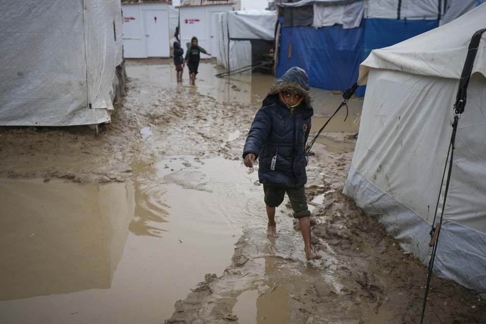 Ein Junge läuft barfuß durch den Schlamm, nachdem es über Nacht in einem Flüchtlingszeltlager für vertriebene Palästinenser geregnet hat.