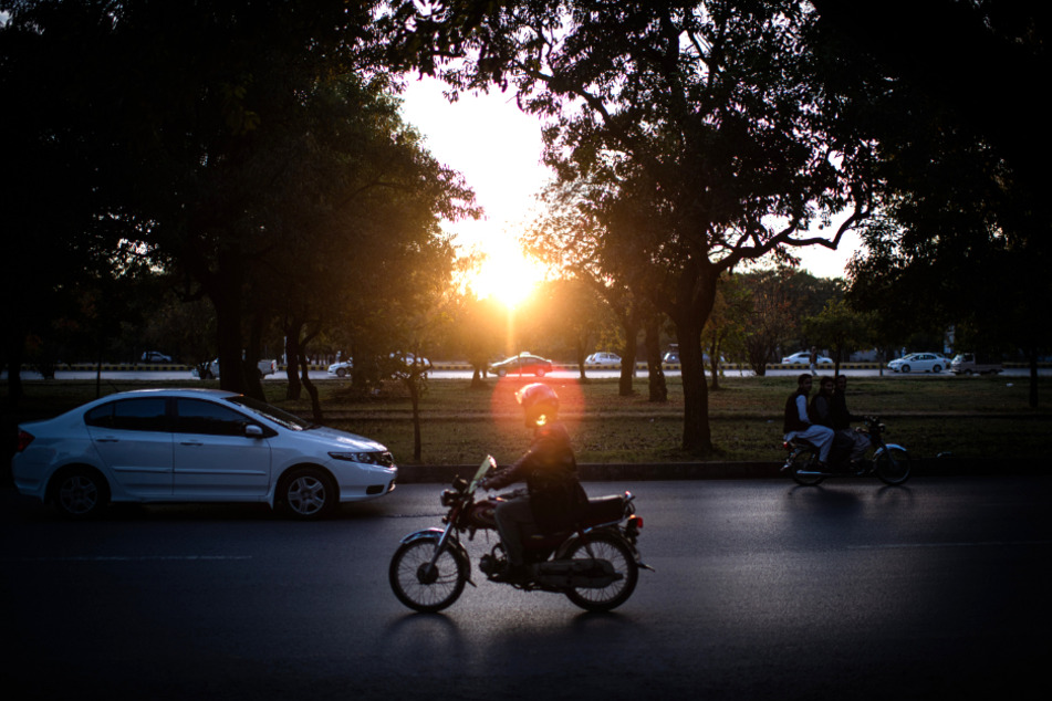 Motorräder und Autos fahren bei herbstlichem Wetter in der pakistanischen Hauptstadt Islamabad bei Sonnenuntergang auf der Straße.