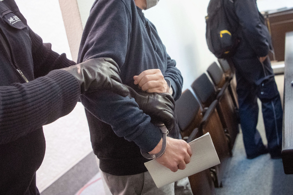 Ein angeklagter Mann (2.vl), der seine frühere Lebensgefährtin mit einem Mitangeklagten in Großaspach entführt und mehr als eine Woche in ihrer Gewalt gehalten haben soll, wird von einem Justizbeamten in einen Gerichtssaal im Landgericht Stuttgart geführt, daneben steht ein weiterer Justizbeamter.