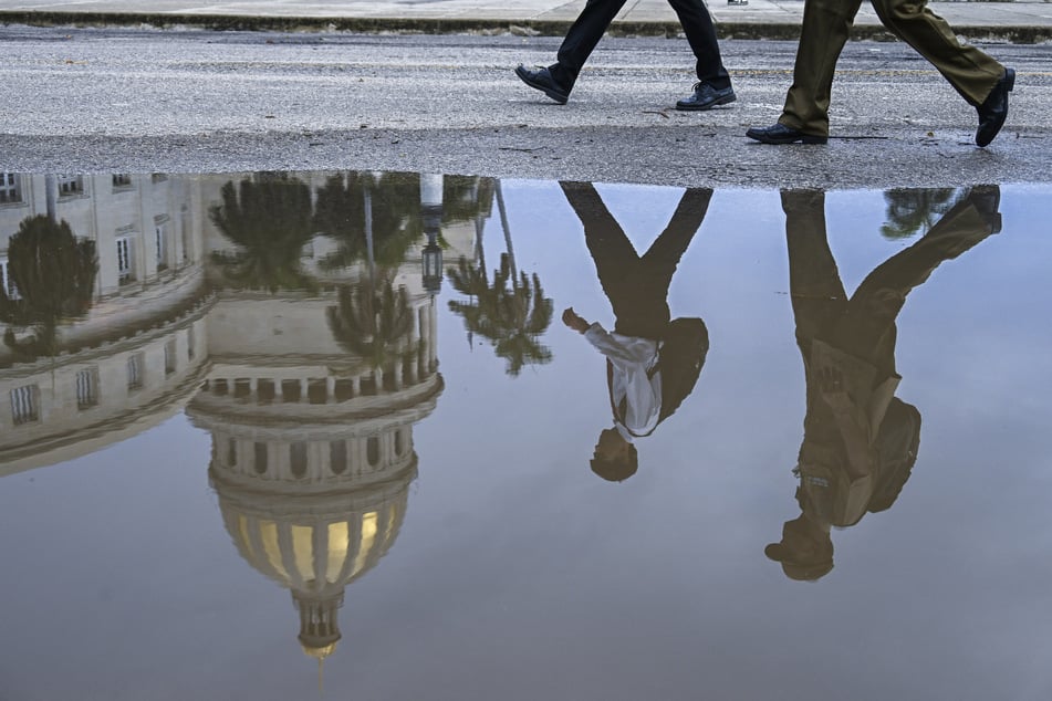 The reflection of pedestrians walking past the Havana Capitol is seen in a puddle in Cuba on July 11, 2026.