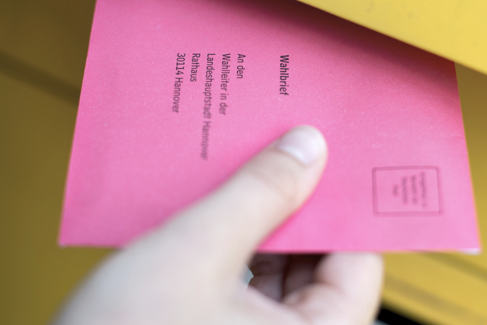 Eine Frau steckt einen Wahlbrief in einen Postkasten.