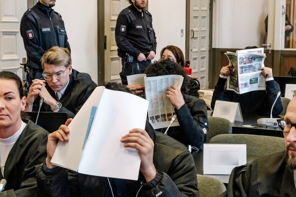 Die Angeklagten verbergen im Gerichtssaal ihre Gesichter. Den insgesamt zehn Männern wird besonders schwerer Raub mit Todesfolge vorgeworfen.