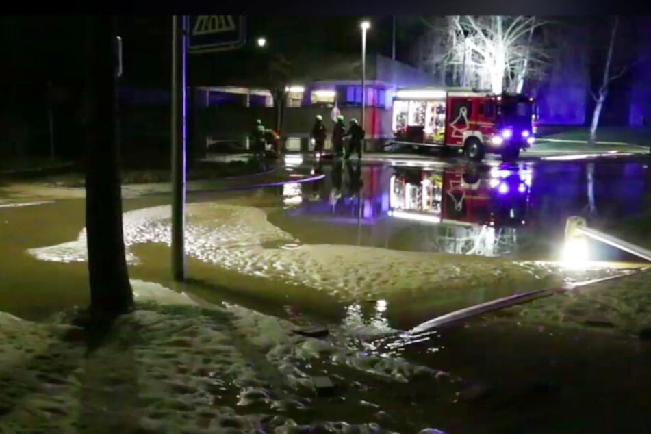 Eine Straße in Lüneburg ist mit Wasser und Sand überflutet, die Feuerwehr pumpt dagegen an.