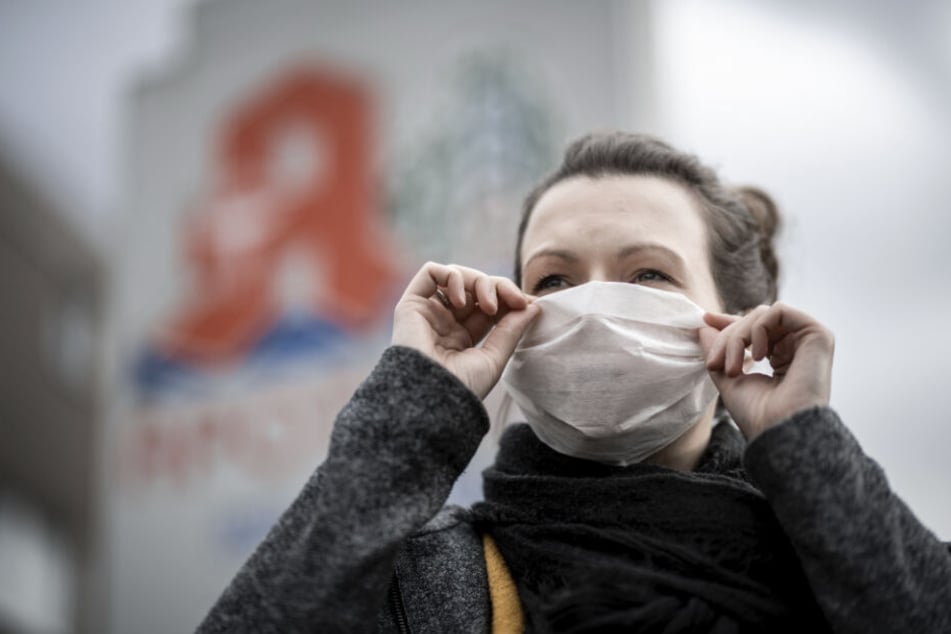 Eine Frau trägt vor einer Apotheke eine Mund- und Nasenmaske.