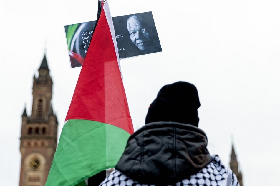 A demonstrator in a keffiyeh raises a Palestinian flag and an image of the late South African President Nelson Mandela during a rally outside the International Court of Justice in The Hague, Netherlands.