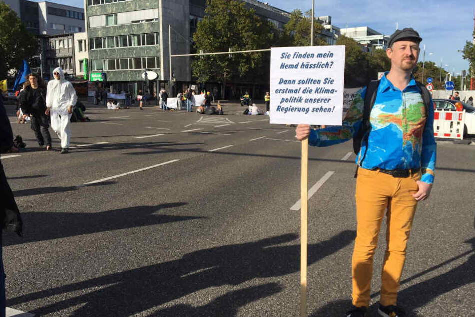 Marco Schlich steht mit seinem Schild auf der Straße.