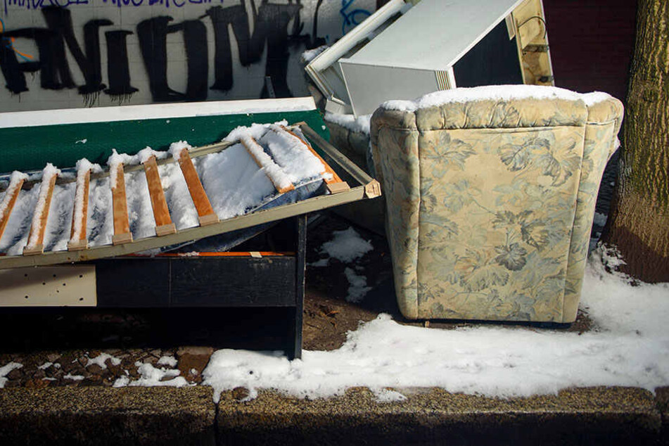 Ein altes Sofa, ein Sessel und ein Bettgestell mit Lattenrost liegen auf einem Gehweg in Berlin-Neukölln im Schnee.