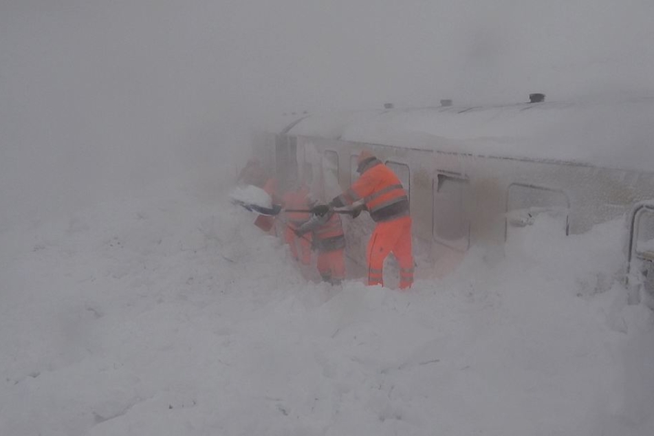 Mehrere Bahnarbeiter schaufeln die vollkommen eingeschneite Bahn frei.