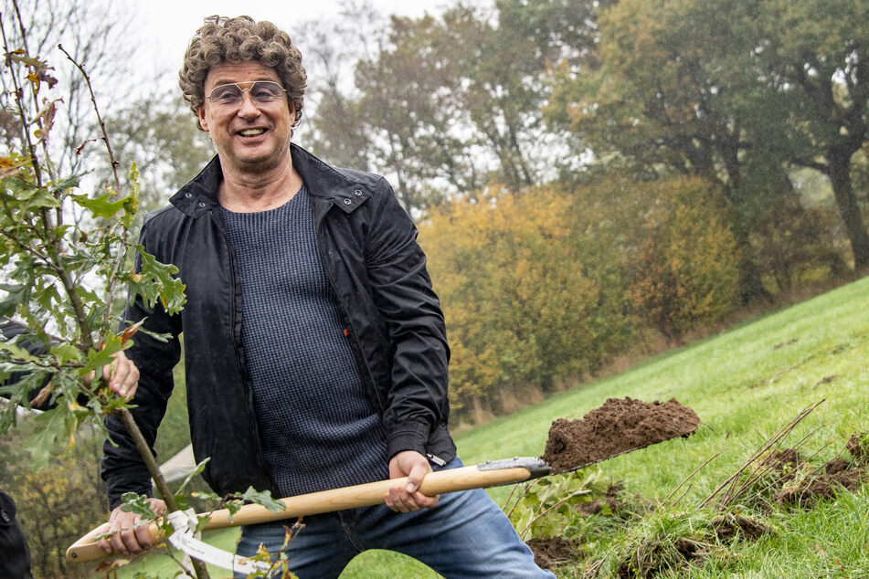 Atze Schröder steht bei der Baumpflanzung mit einem Spaten in der Hand auf einem Feld.