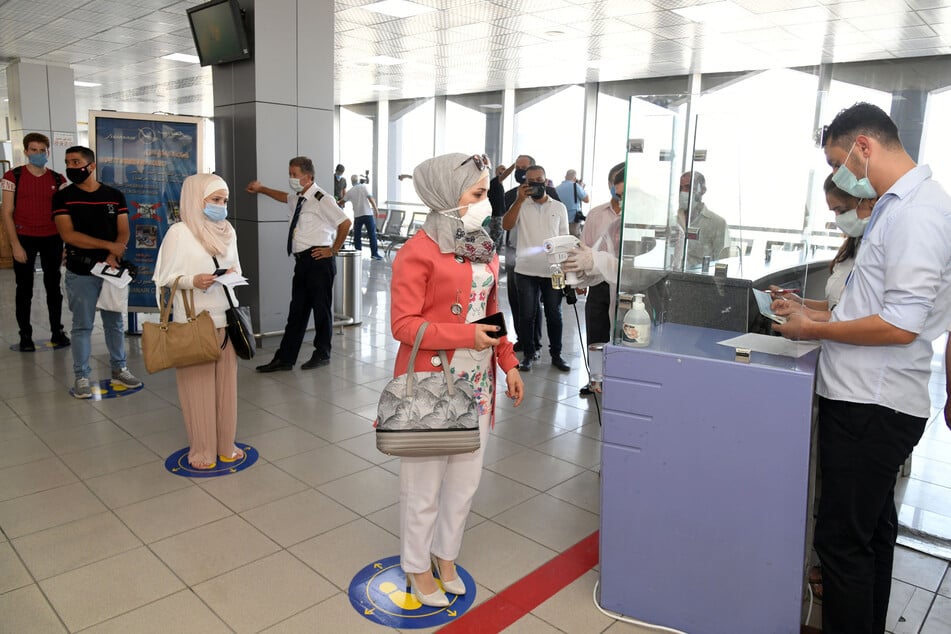 Passagiere tragen Schutzmasken und stehen auf dem Internationalen Flughafen in Damaskus.