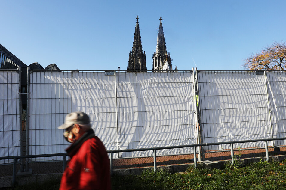 Ein Mann geht an Absperrgittern vorbei, die in der Nähe des Domes stehen.