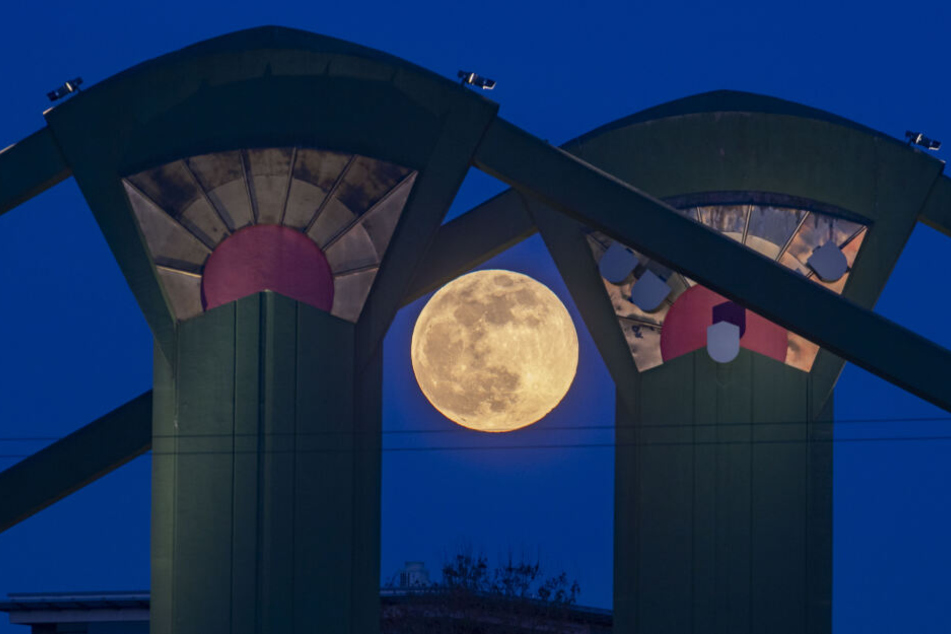 Der Vollmond zwischen den beiden farbig gestrichenen und illuminierten Betonträgern der Flößerbrücke in Frankfurt am Main.