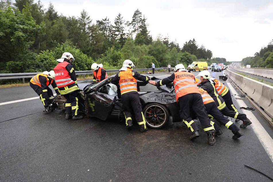 Die Kameraden der Feuerwehr schieben den demolierten Porsche von der Fahrbahn.