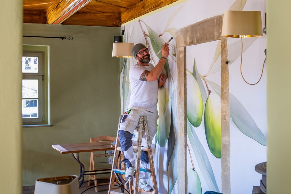 Malermeister René Kunst (47) bessert noch einige Stellen an seiner "Olivenwand" aus. Die ehemals schwarze Decke hat er in Holzoptik gemalt.