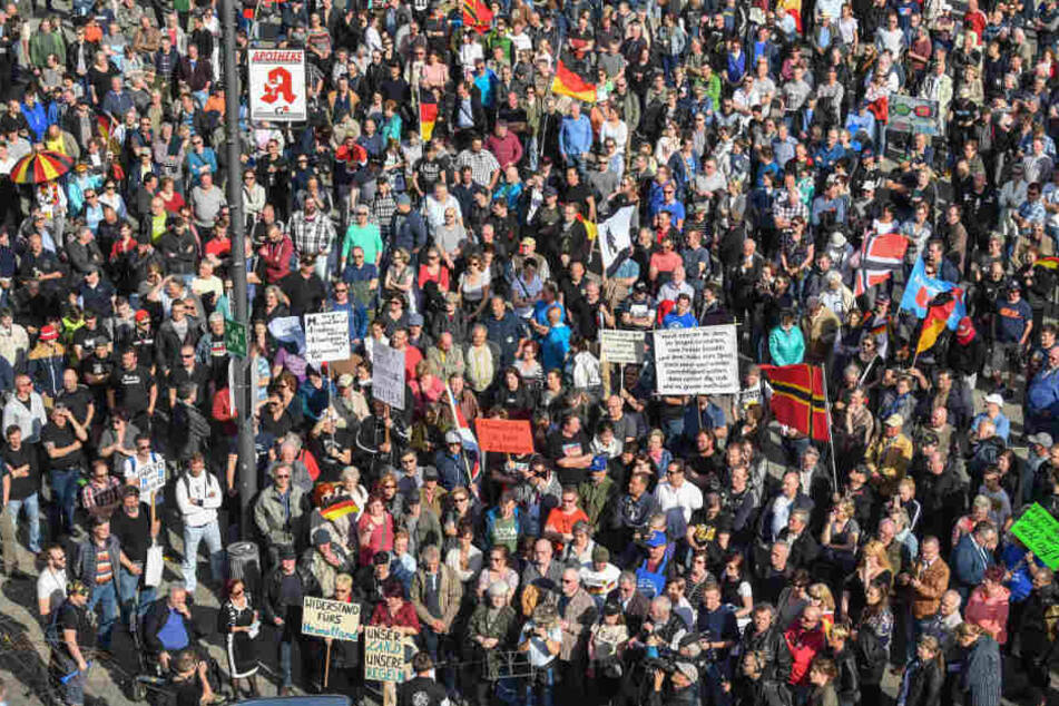 Viele Demonstranten stehen mit Transparenten und Fahnen auf einem Platz vor der Stadthalle von Cottbus und protestiert gegen Zuwanderung und die Asyl-Politik der Bundesregierung.