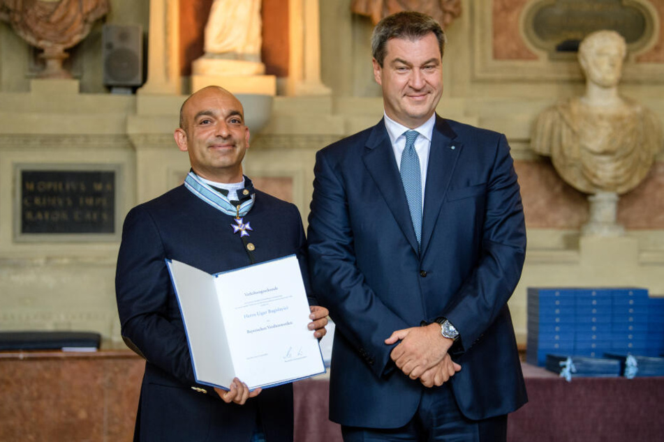 Markus Söder (CSU, r), Ministerpräsident von Bayern, überreicht im Antiquarium der Residenz Django Asül, Kabarettist, Autor und Kolumnist, bürgerlich Ugur Bagislayici, seine Auszeichnung mit dem Bayerischen Verdienstorden. (Archivbild)