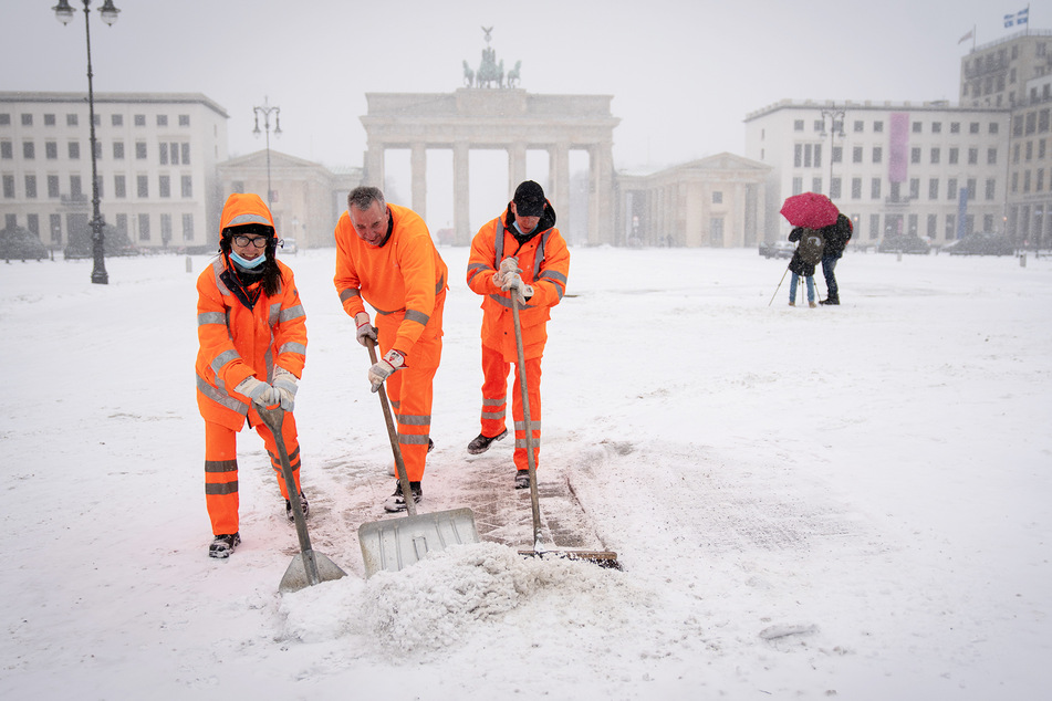 Mitarbeiter der Berliner Stadtreinigung schaufeln den Schnee am Brandenburger Tor vom Gehweg.