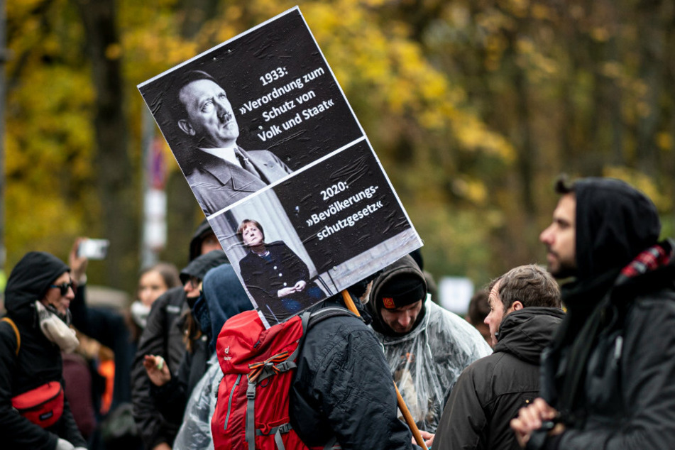 Ein Teilnehmer der Demonstration gegen die Corona-Einschränkungen hält ein Schild hoch auf dem unter Adolf Hitler Angela Merkel abgebildet ist.